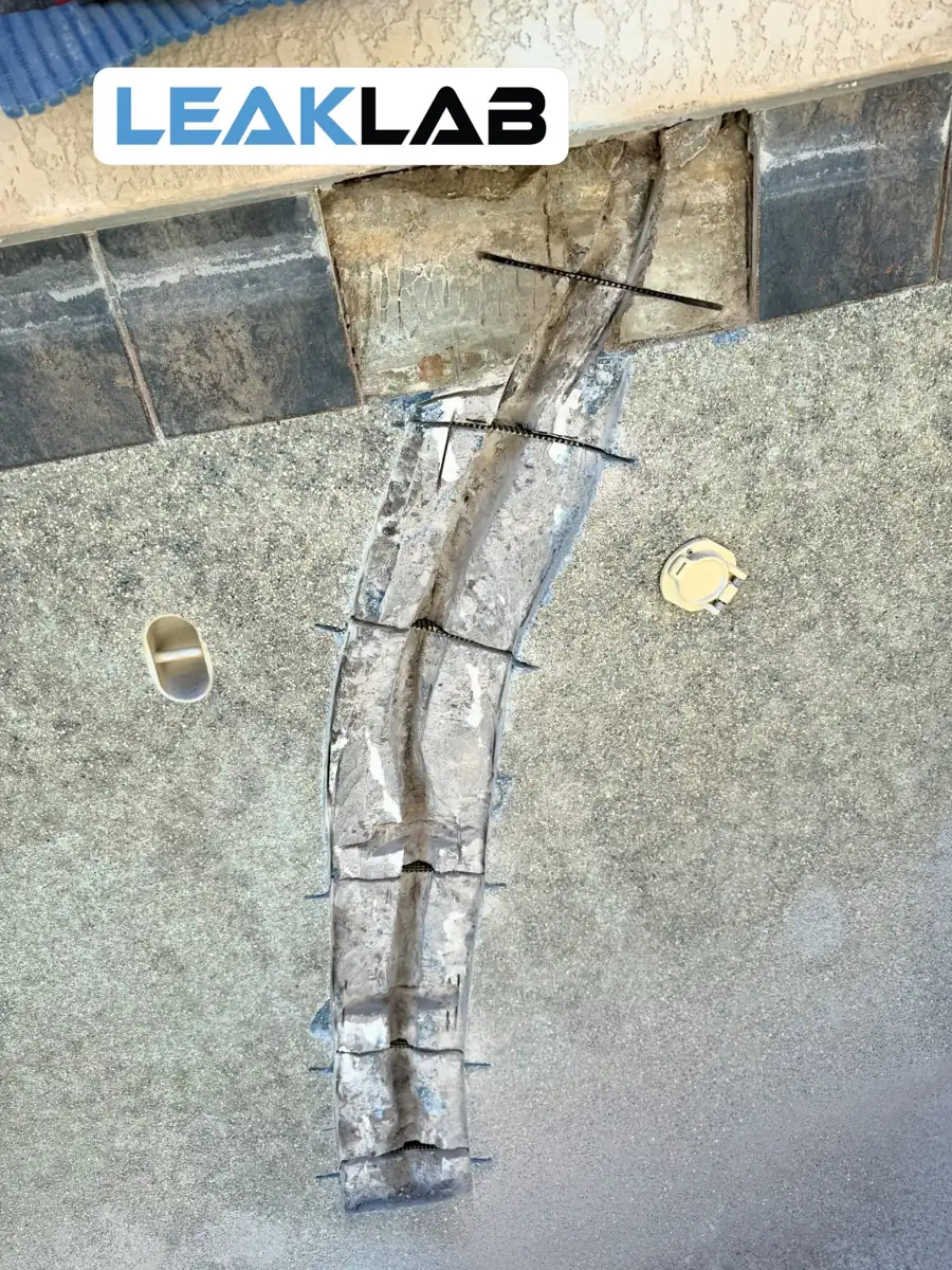 Staples set across a pool wall crack with waterline tile removed to reach the bond beam